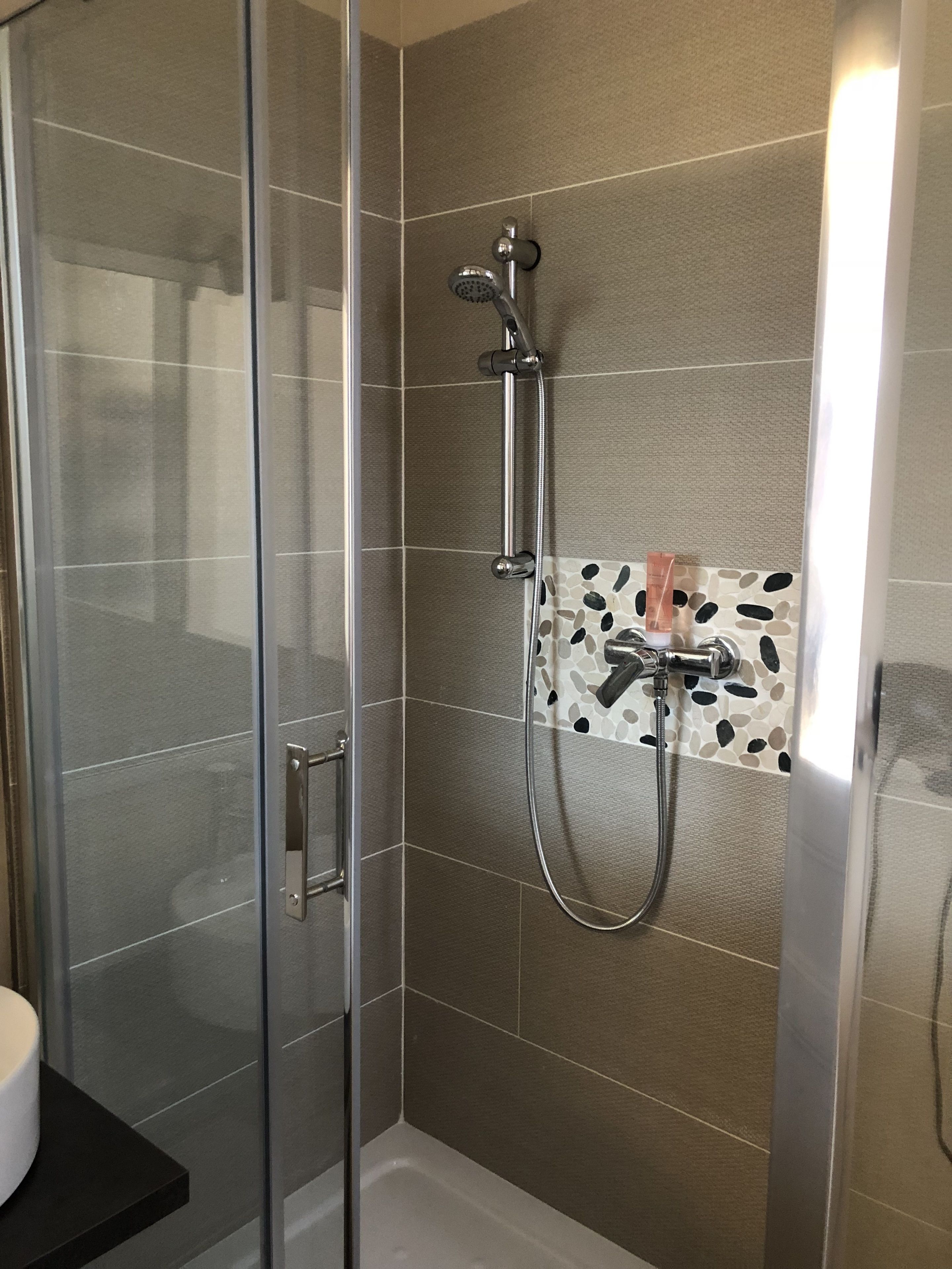 Een douchecabine van glas met een handdouche en een wandmengkraan.