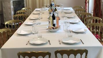 Una larga mesa de comedor con mantel blanco, platos, vasos y botellas, rodeada de sillas de madera.