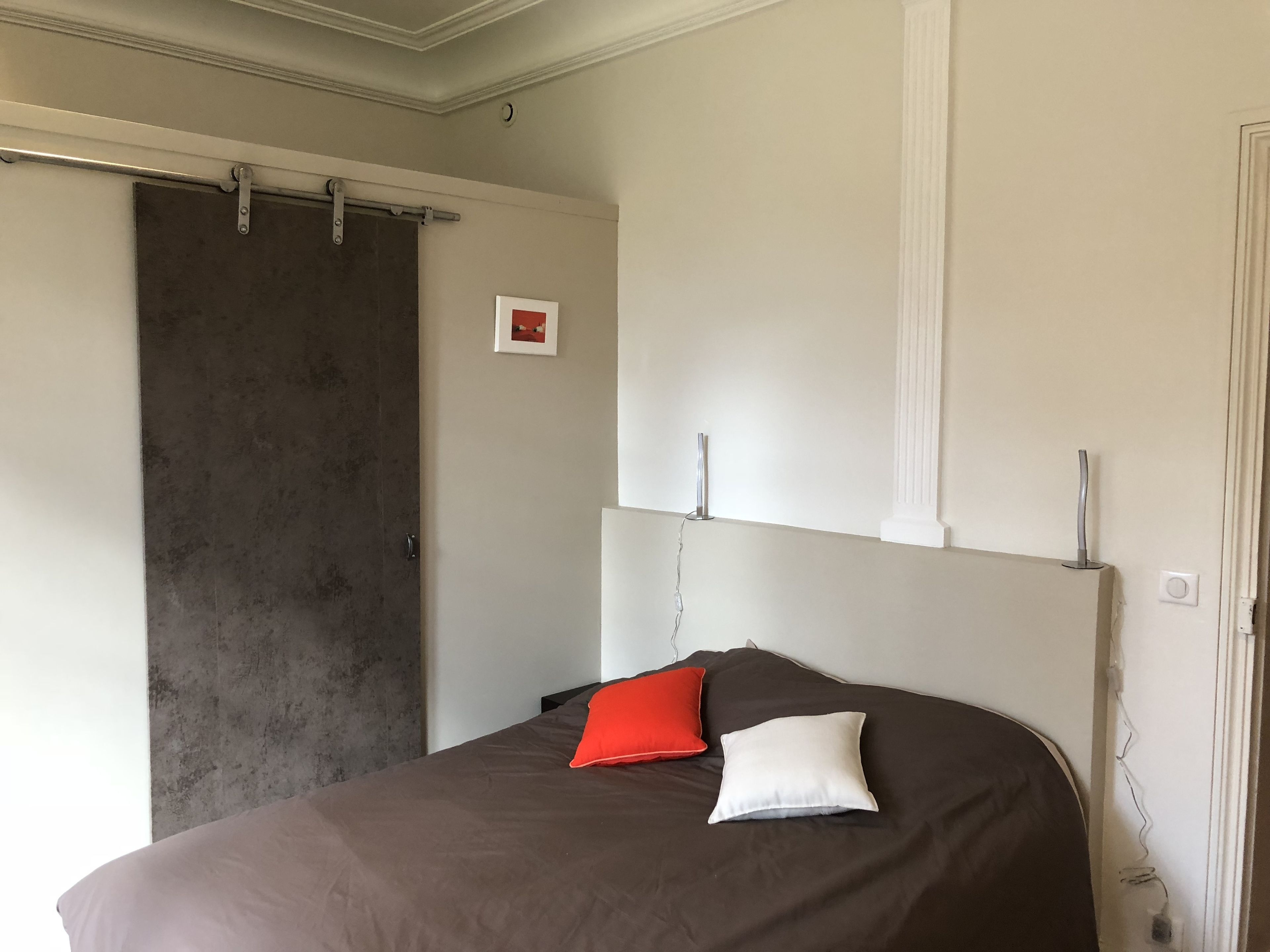 A bedroom with a bed, a sliding door, a framed picture, and a white wall.