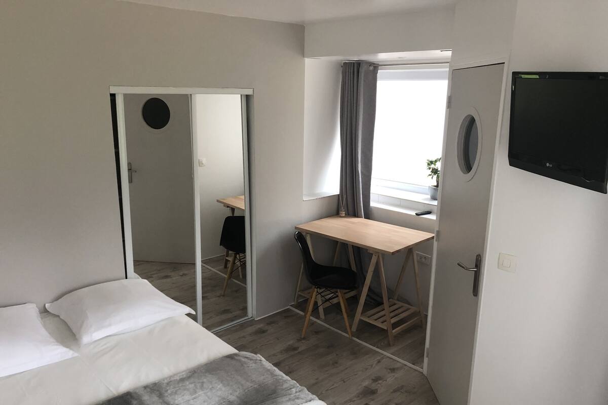 Une chambre d’hôtel avec un lit, un bureau, une chaise, un miroir et un téléviseur.