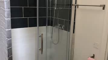 A glass-enclosed shower with a white toilet and a black tiled wall.