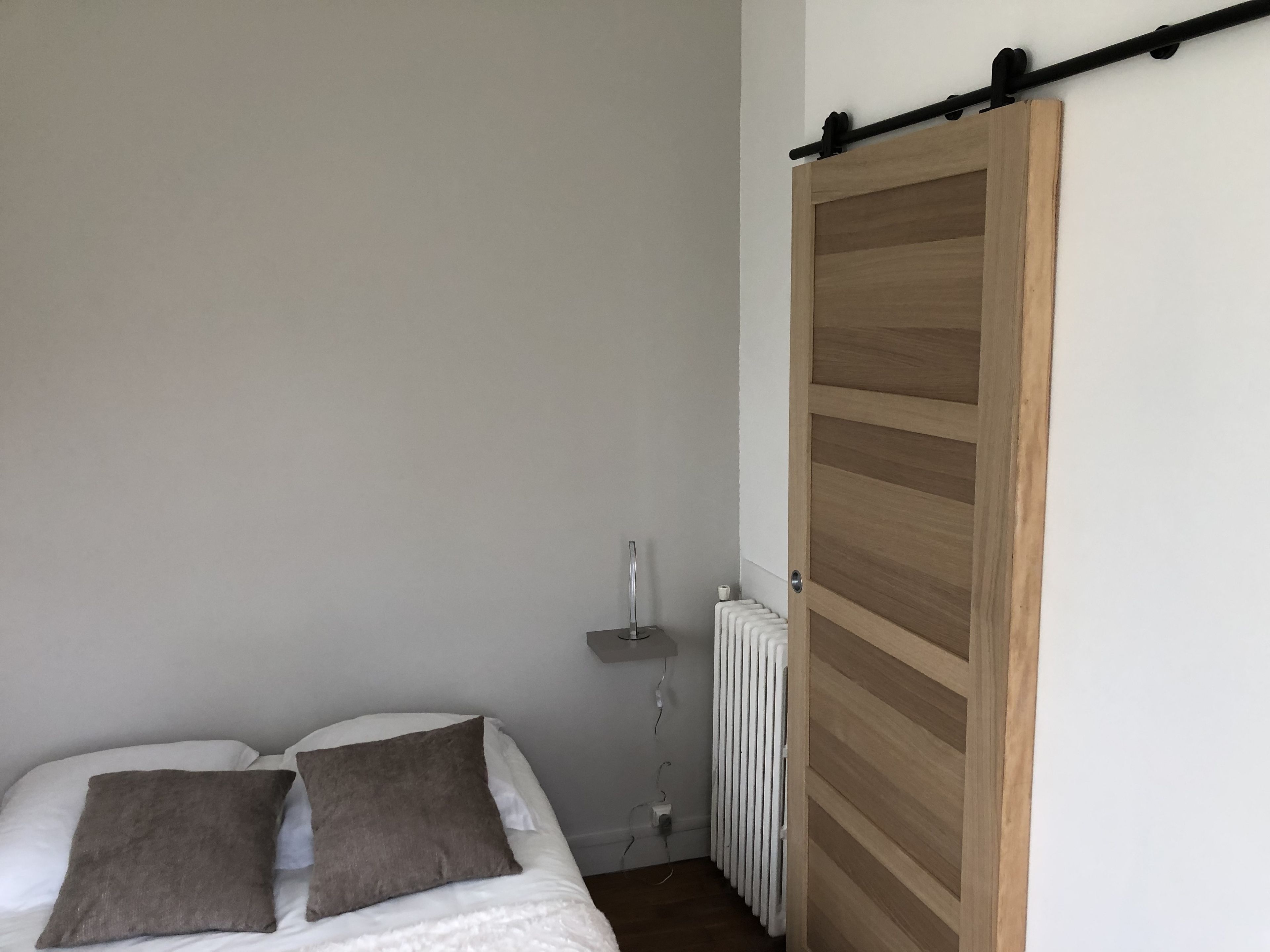 A bedroom with a bed, two pillows, a radiator, and a sliding wooden door.