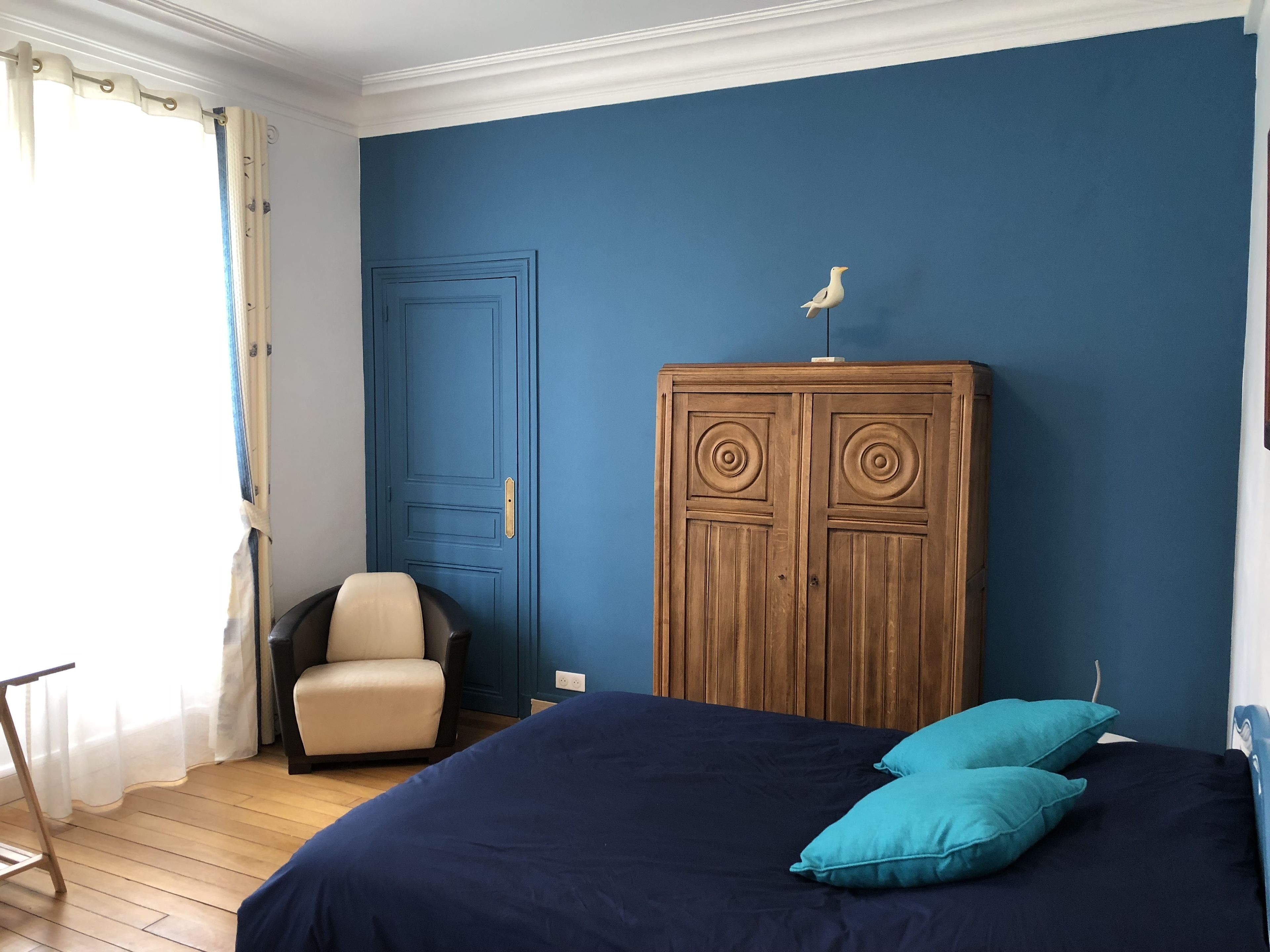 Un dormitorio con una cama grande, un armario de madera, una silla y un ventanal con cortinas.