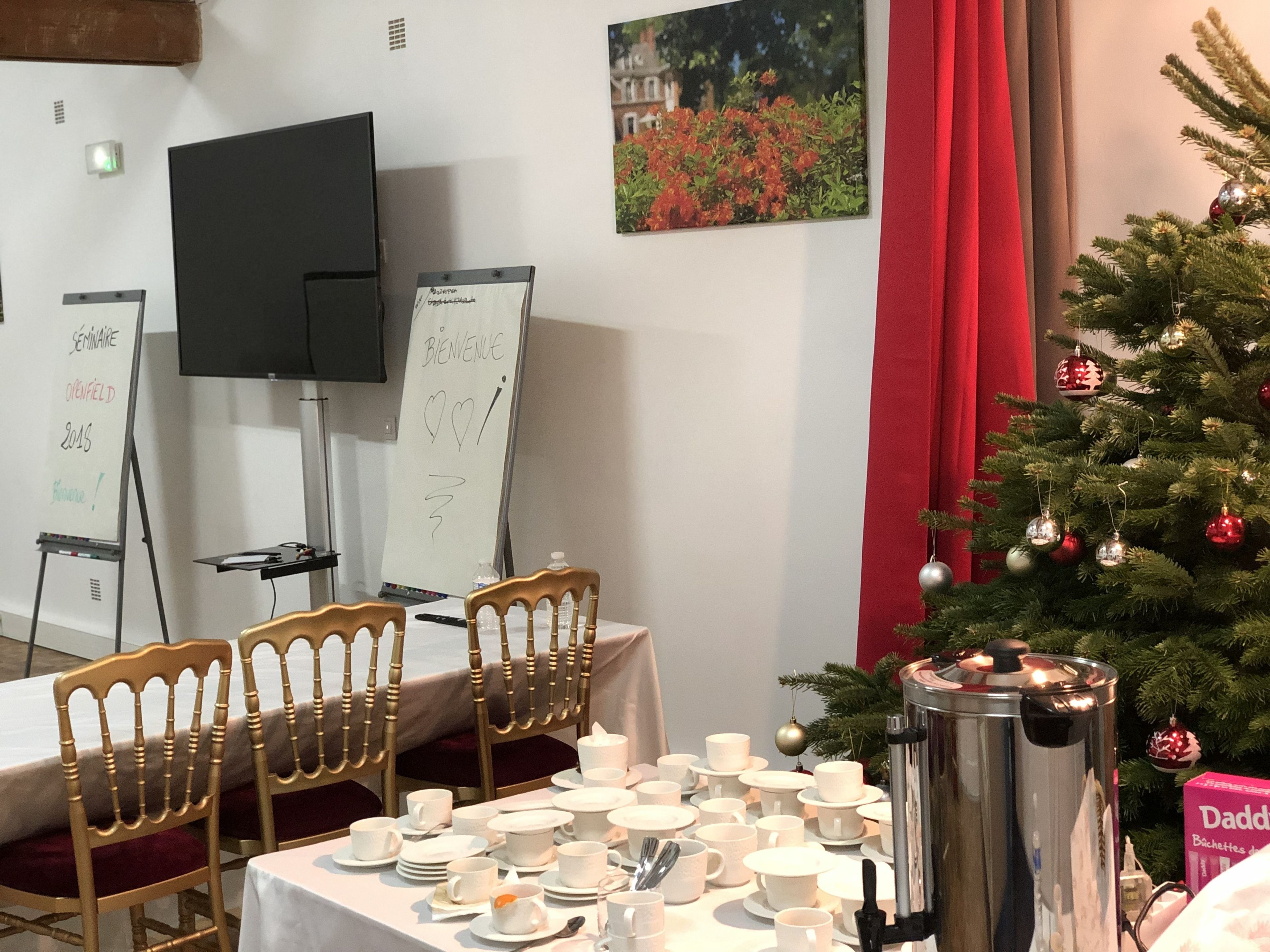 A dining area with a Christmas tree, white tablecloths, and a coffee pot.