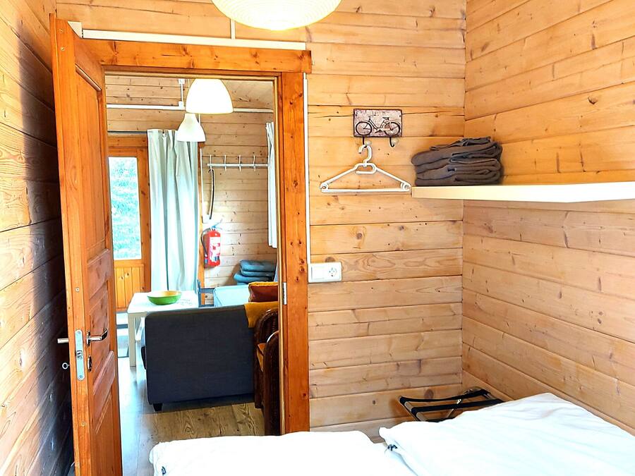 Una habitación de cabaña de madera con una cama, una lámpara colgante, una mesita con una silla y una bicicleta como adorno en la pared.