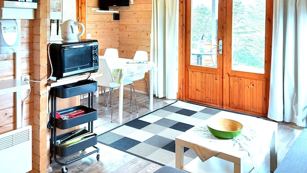 A wooden cabin interior with a dining area, kitchenette, and a large window. - Ásgeirsstaðir Cottages (Eidar)