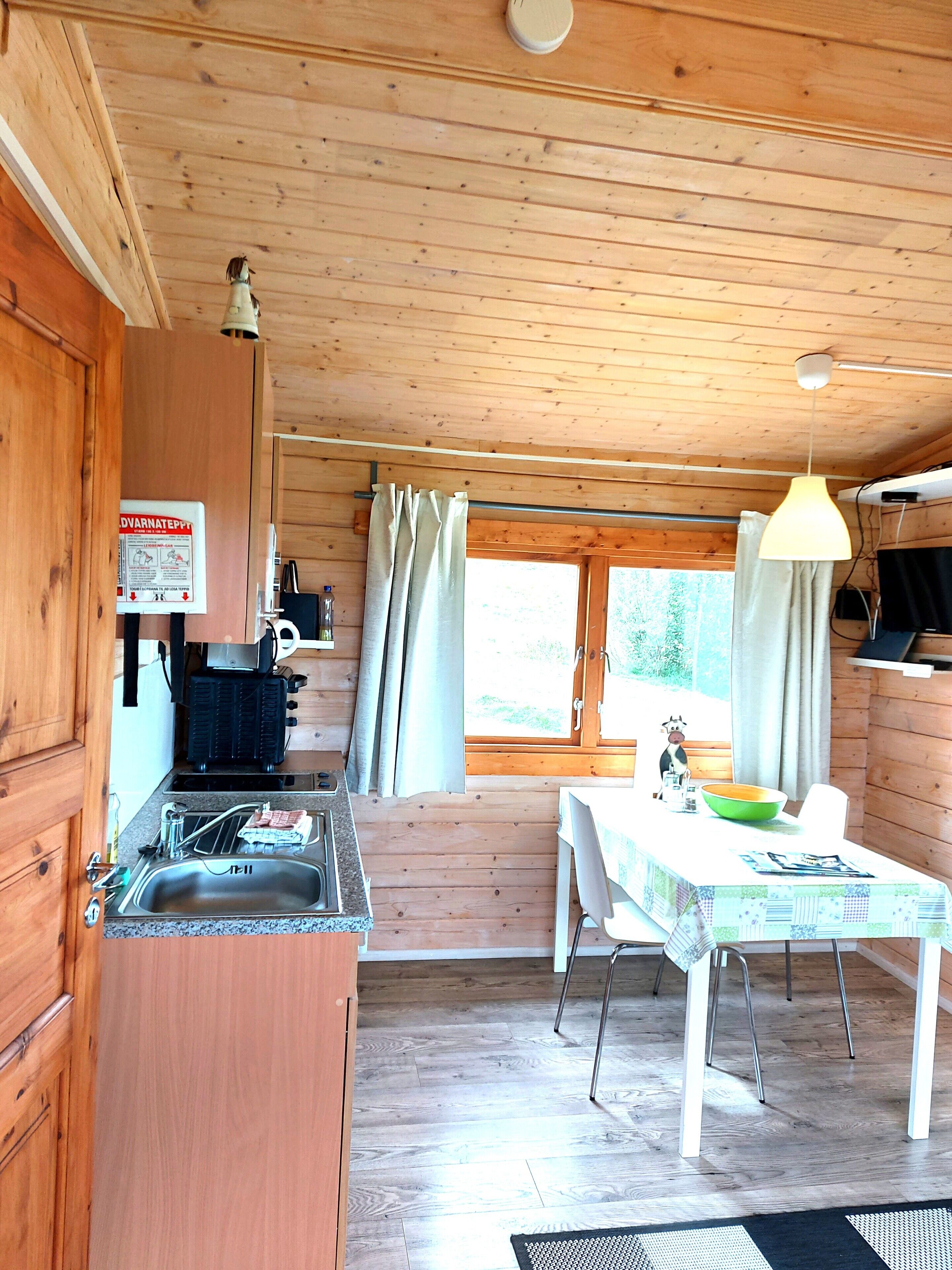 A wooden cabin kitchen with a dining area, a sink, a stove, and a window with curtains.