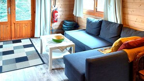 A cozy cabin interior with a sofa, a small table, a hanging light, and a window with curtains. - Ásgeirsstaðir Cottages (Eidar)