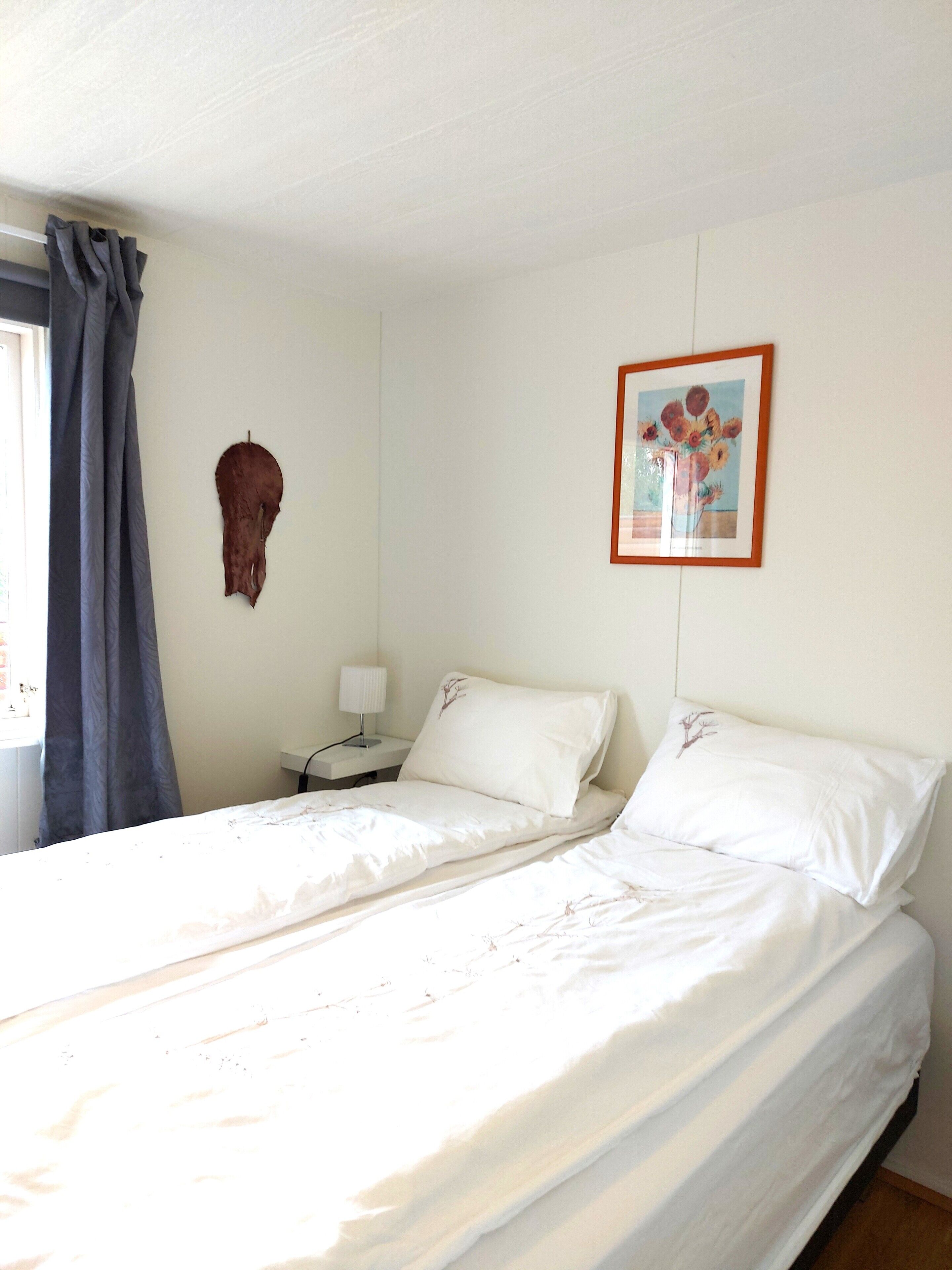 A bedroom with two beds, a nightstand with a lamp, a framed picture on the wall, and a curtain.