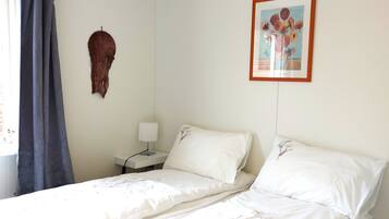 A bedroom with two beds, a nightstand with a lamp, a framed picture on the wall, and a curtain.