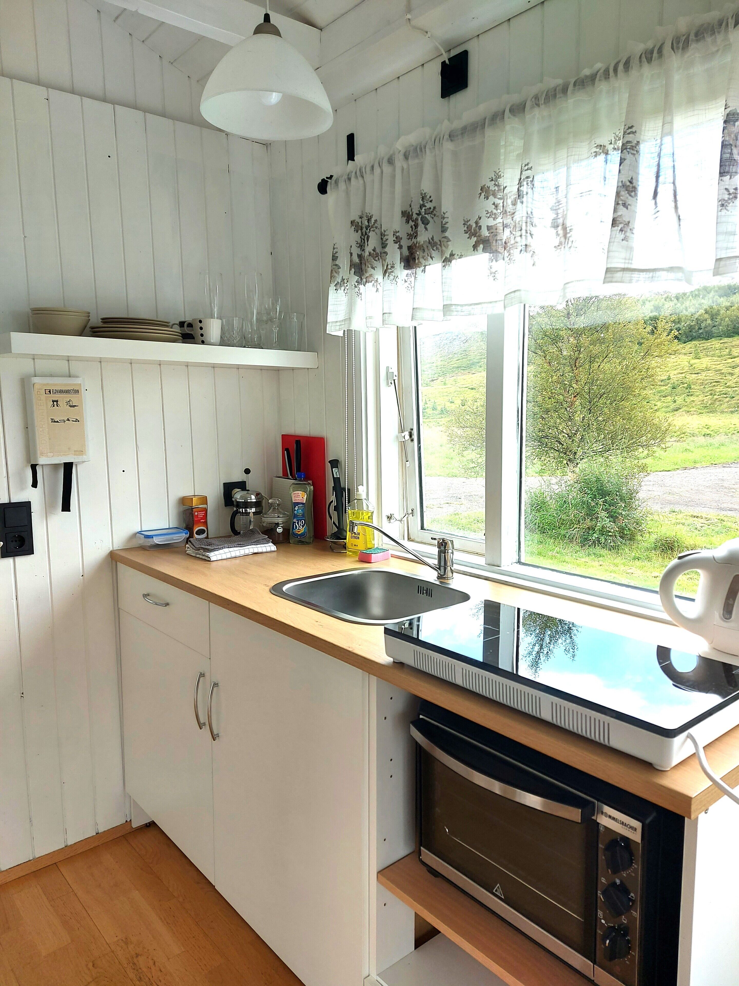 A kitchen with a sink, stove, and window with a view of greenery.