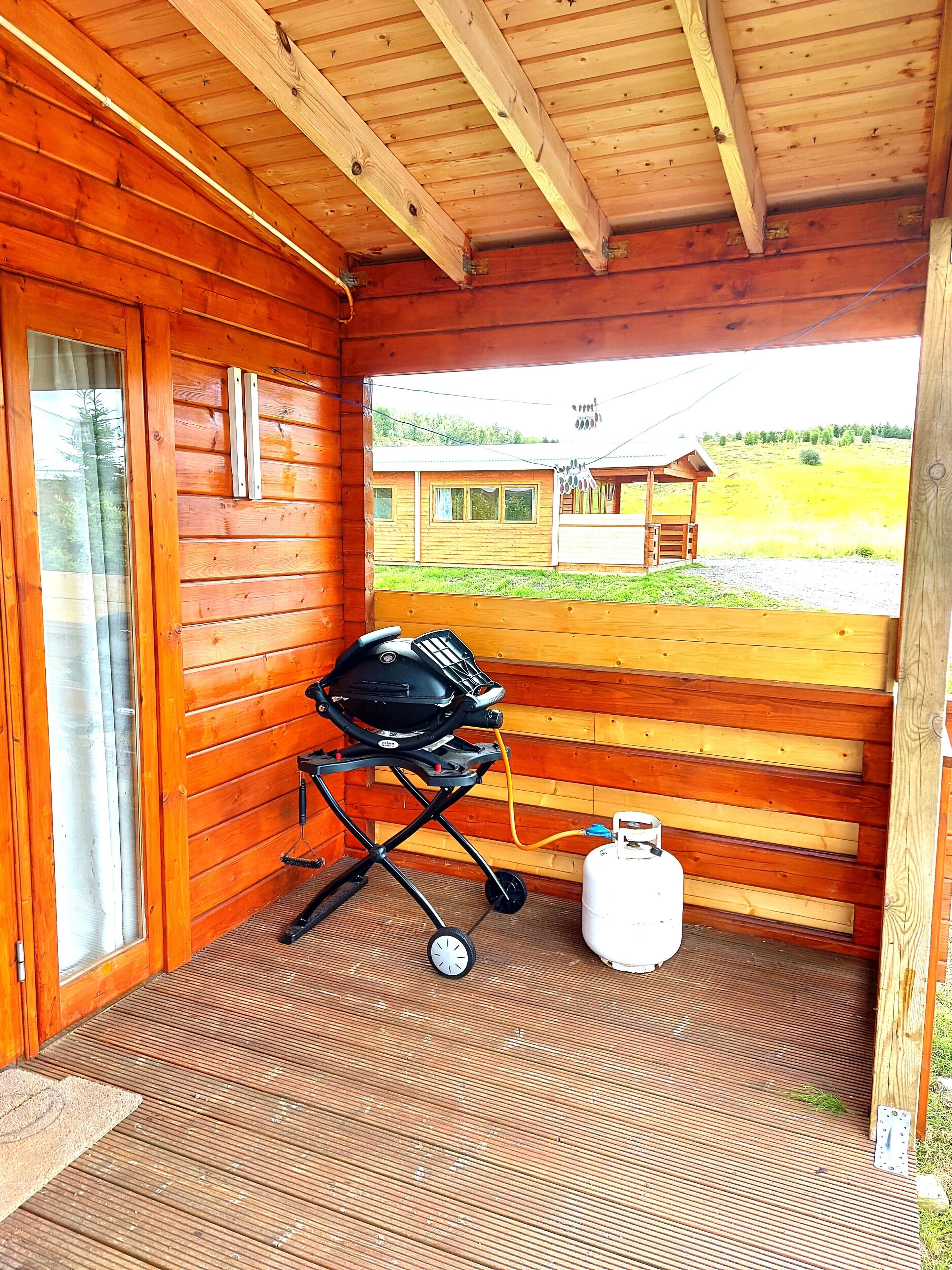 A wooden cabin with a covered porch, a grill, and a propane tank.