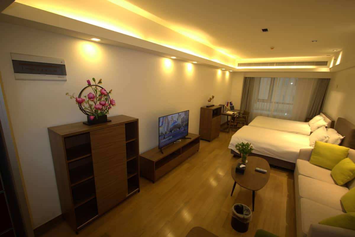 A hotel room with a bed, a TV, a desk, a sofa, and a small table with a plant.