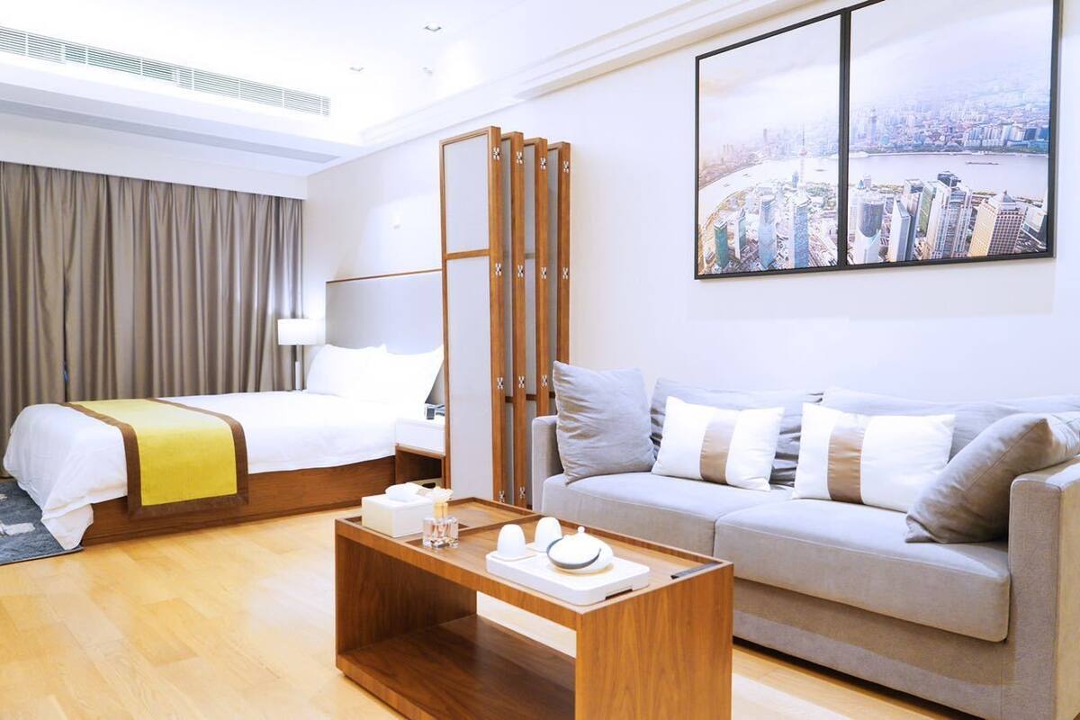 A hotel room with a bed, a sofa, a coffee table, and a cityscape view.