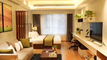 A modern hotel room with a bed, sofa, desk, TV, and potted plants.