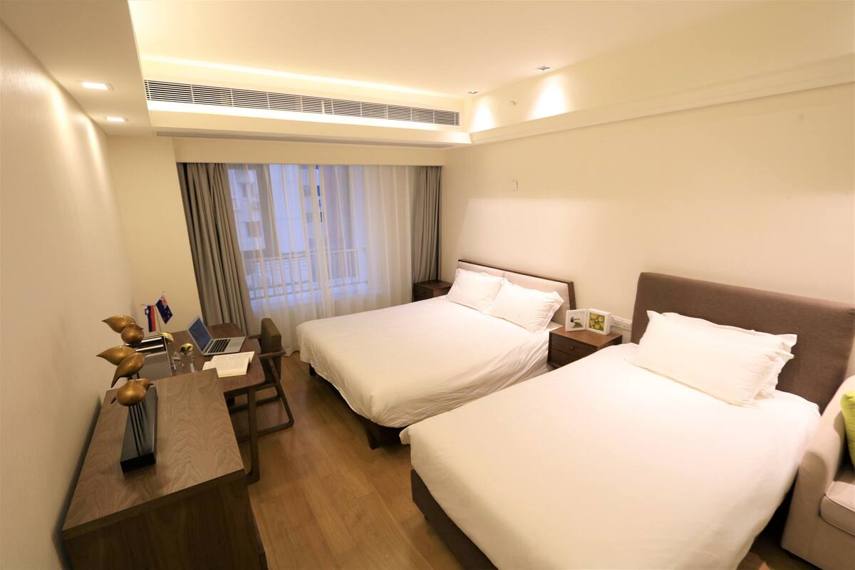 A hotel room with two beds, a desk with a laptop, a chair, and a small table with decorative items.