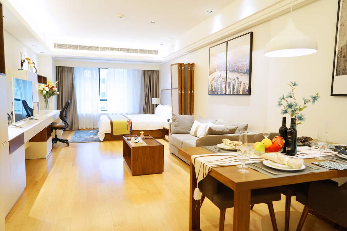 A modern hotel room with a dining area, a bed, a desk, and a view of the city.