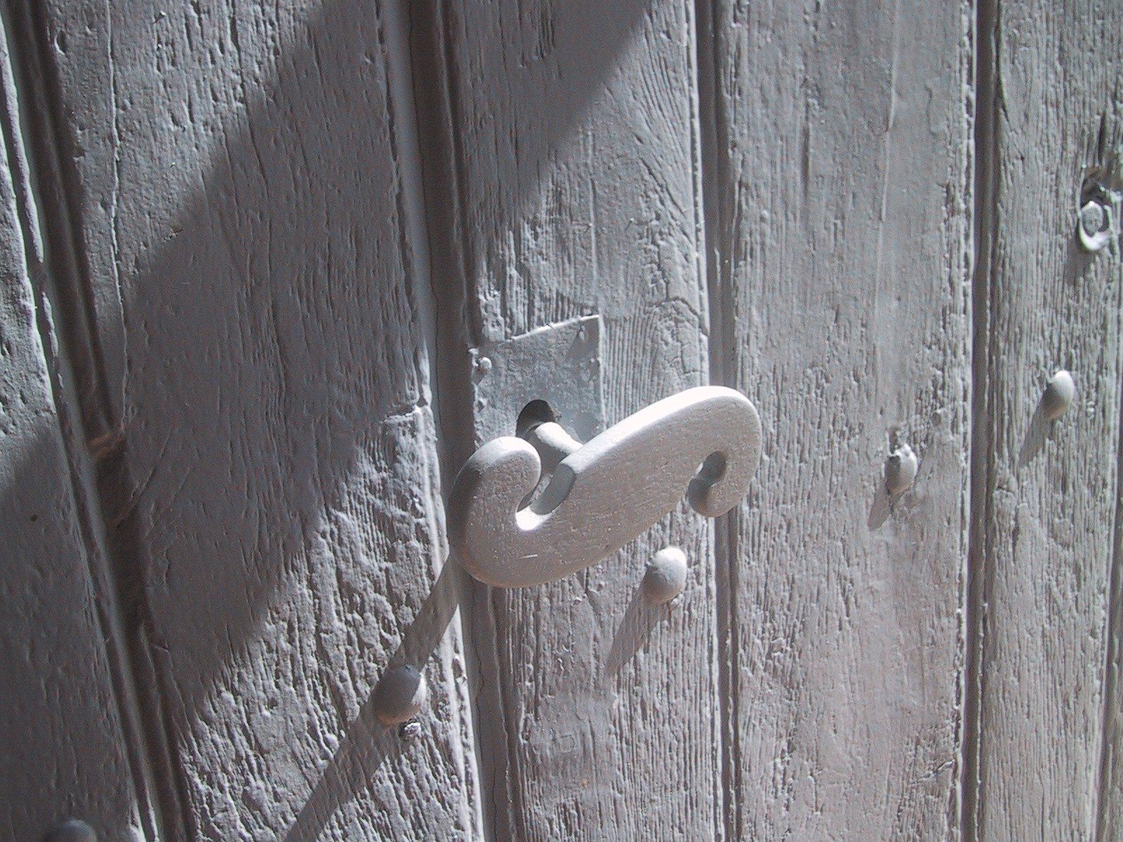 Une porte en bois usée par les intempéries, dotée d’une poignée en métal et d’une petite fenêtre carrée.