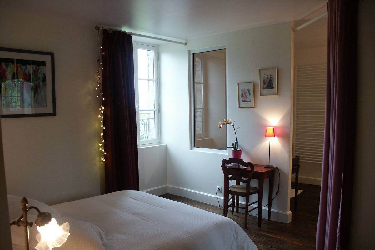 A bedroom with a bed, a desk, a chair, a lamp, and a window with curtains.