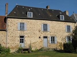 Un bâtiment en pierre doté de nombreuses fenêtres et d’une porte, entouré d’une zone herbeuse et de quelques plantes.
