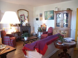 Un salon chaleureux avec une cheminée, des meubles à motifs écossais et un grand meuble en bois.