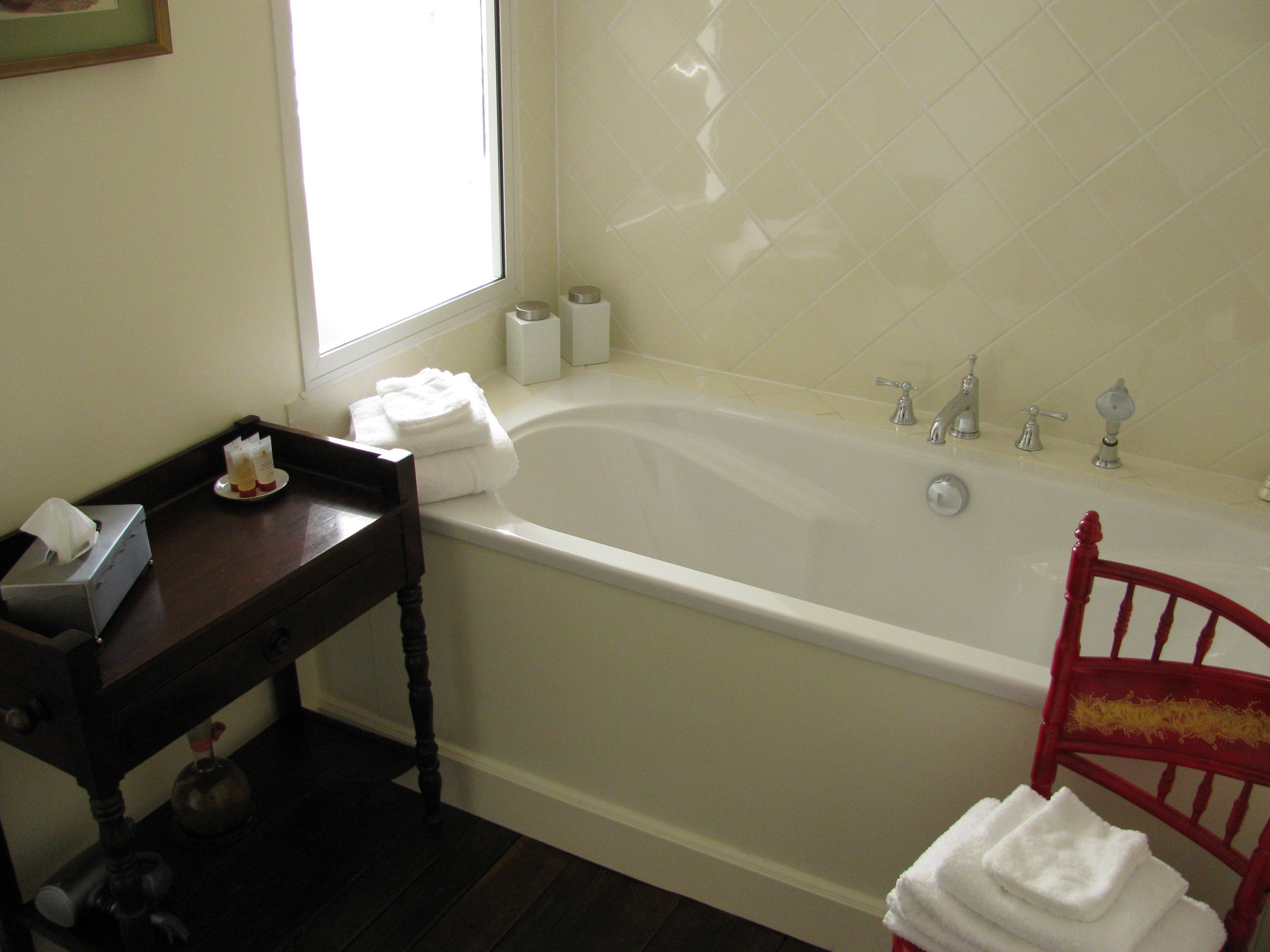 Un baño con una bañera, una mesa de madera con artículos de aseo, y una silla roja.