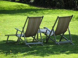 Deux fauteuils de jardin, dotés d’une structure en métal et d’un tissu à rayures, sont placés sur une pelouse verdoyante parsemée de pissenlits.