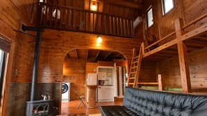 Acogedor interior de cabaña con chimenea, un sofá, cocina y un altillo.
