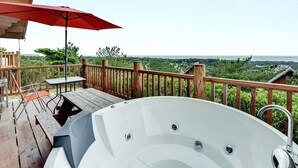 Una terraza de madera con un jacuzzi, una mesa y un paraguas rojo.