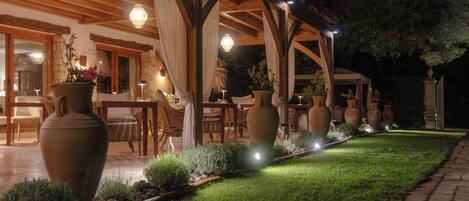 Un espace extérieur aménagé en terrasse, avec des poutres en bois, de grands vases et un chemin de jardin bien éclairé.