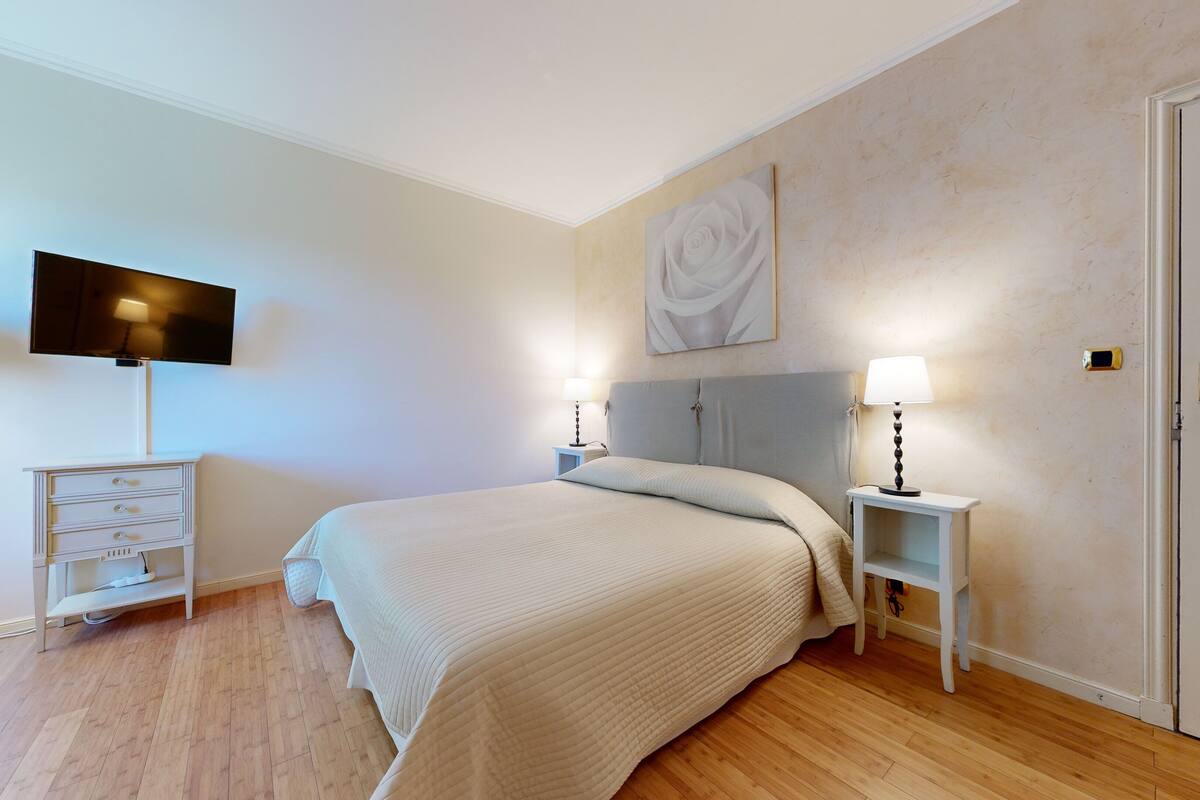 A bedroom with a bed, bedside tables, a TV, and a door with a lock.
