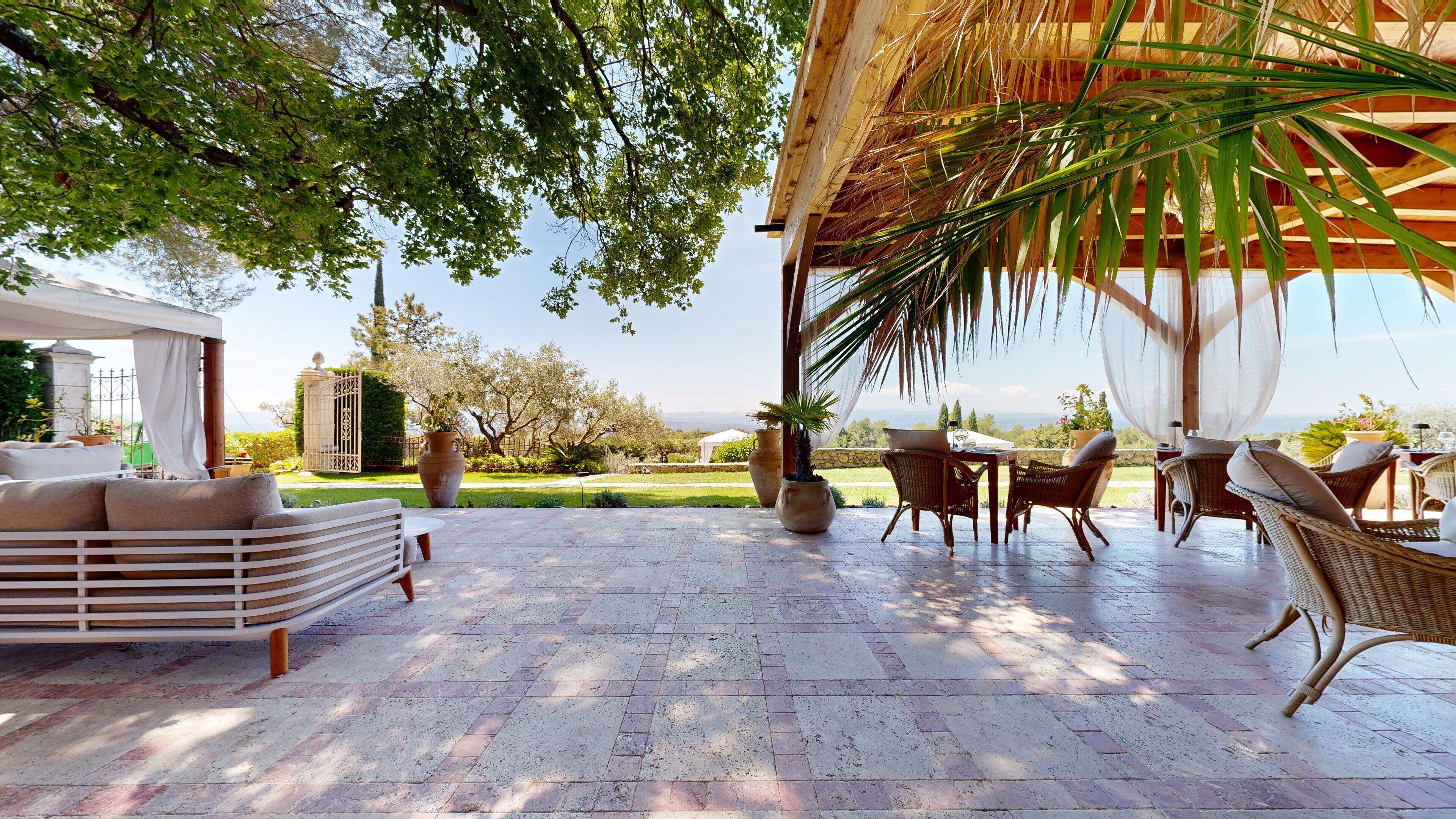 A covered outdoor seating area with wicker furniture, a pergola, and a view of a landscaped garden.