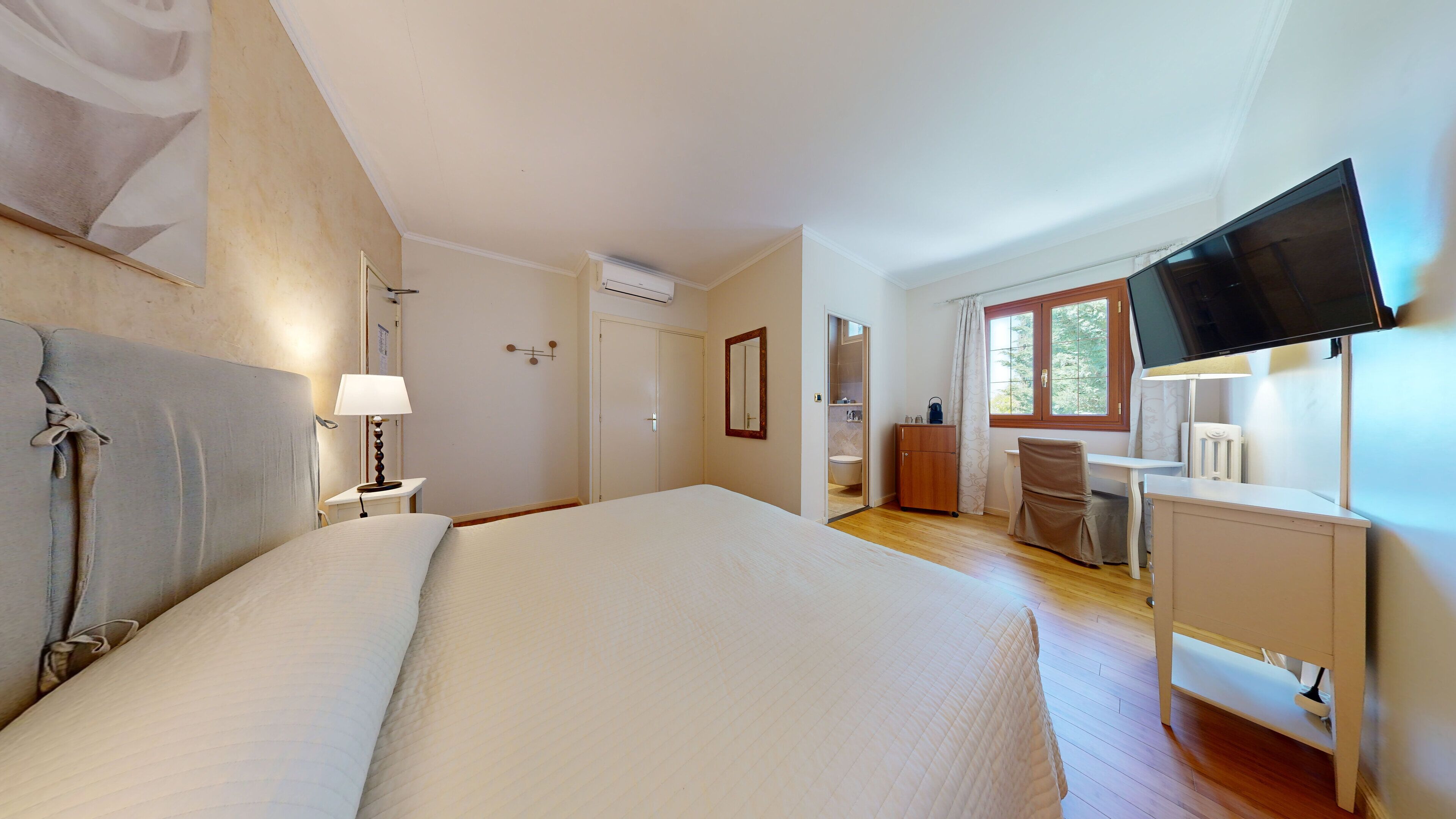 A bedroom with a large bed, a desk, a chair, a television, and a bathroom visible through an open door.