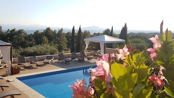 Ein Poolbereich mit Liegestühlen und einer Pergola, umgeben von Grün und Blick auf ferne Berge.