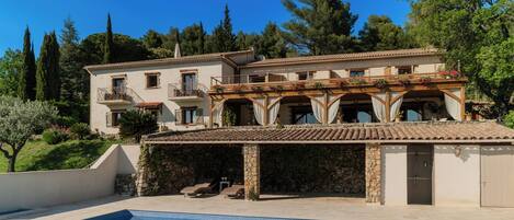 A two-story building with a swimming pool, stone pillars, and a balcony with potted plants.