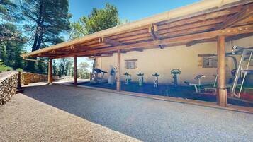 Un espace de remise en forme extérieur abrité, équipé de matériel d’exercice, avec un mur en pierre et une vue sur les arbres.