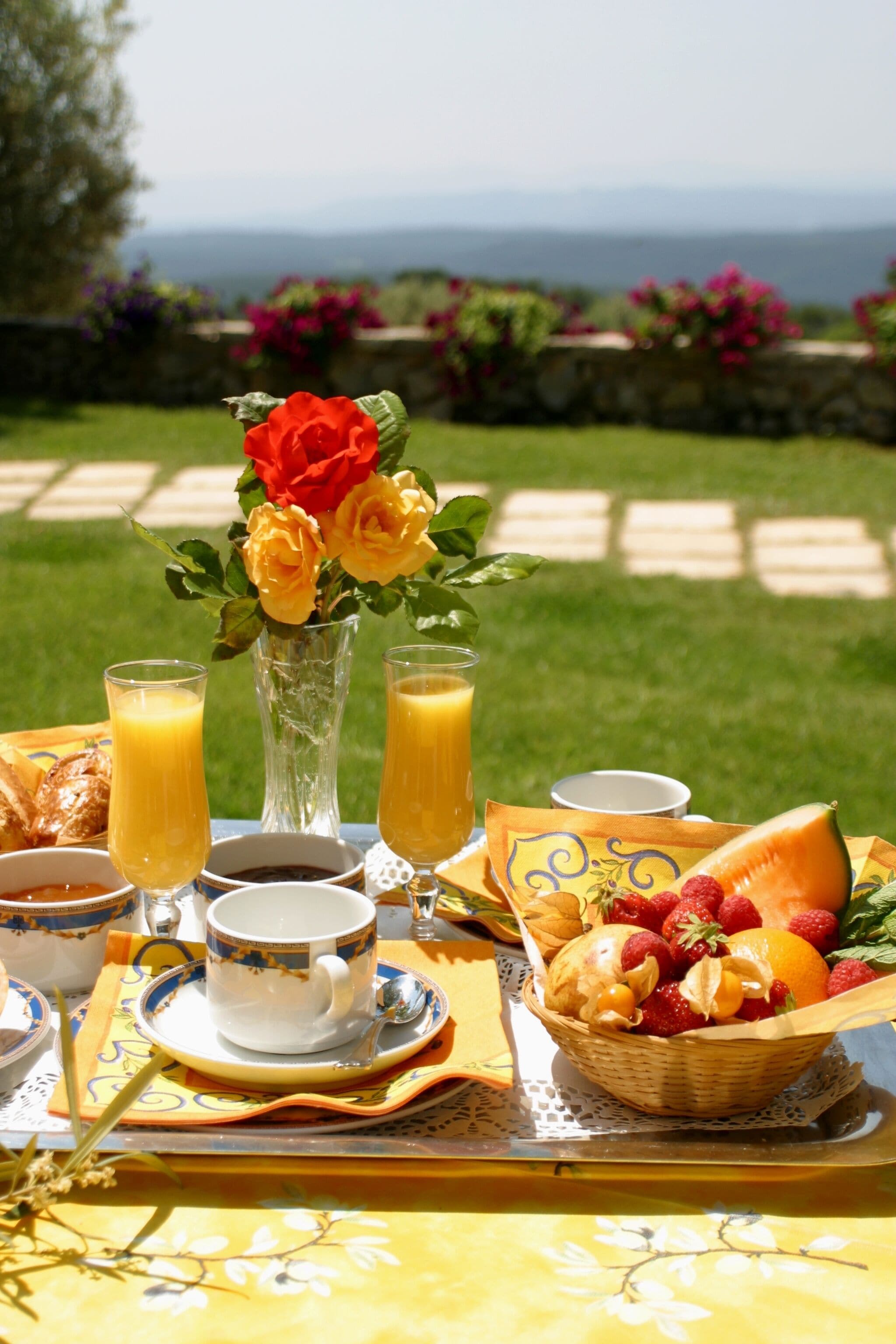 A breakfast setup with a table, a vase of flowers, and a basket of fruit.