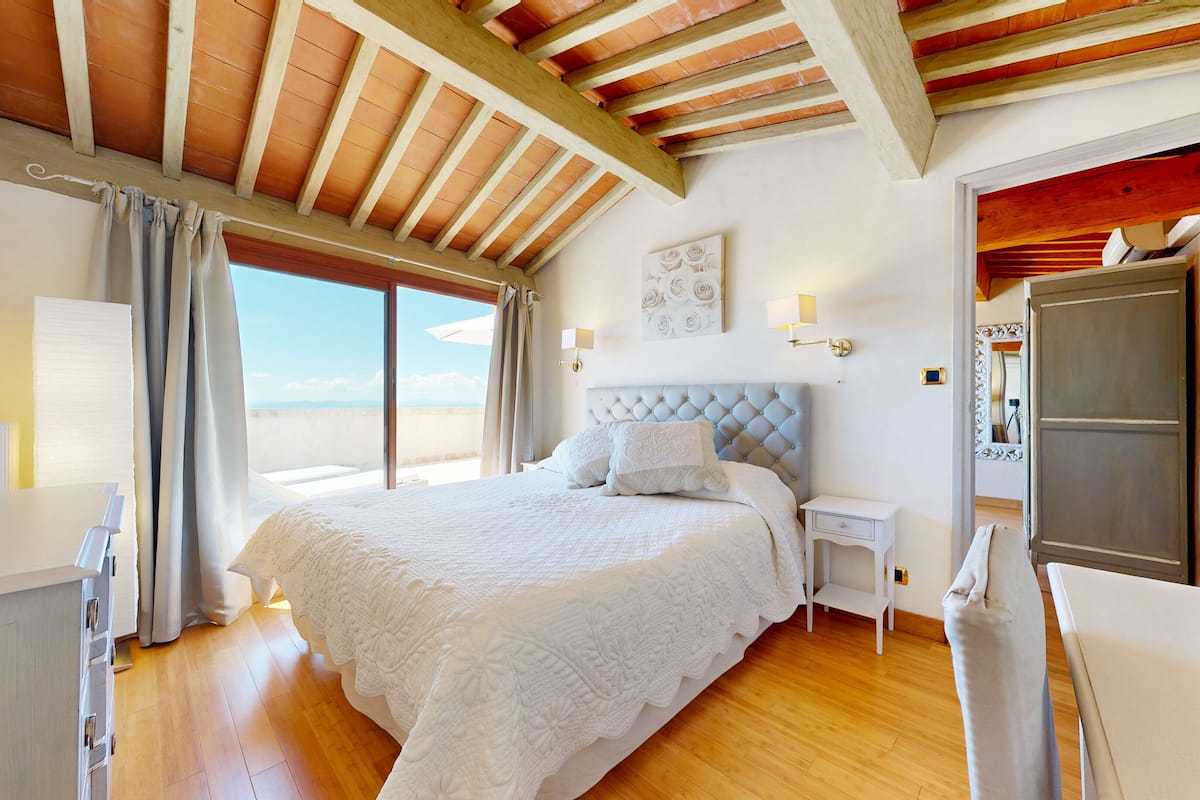 A bedroom with a large bed, a wooden ceiling, a view of the sky, and a white dresser.