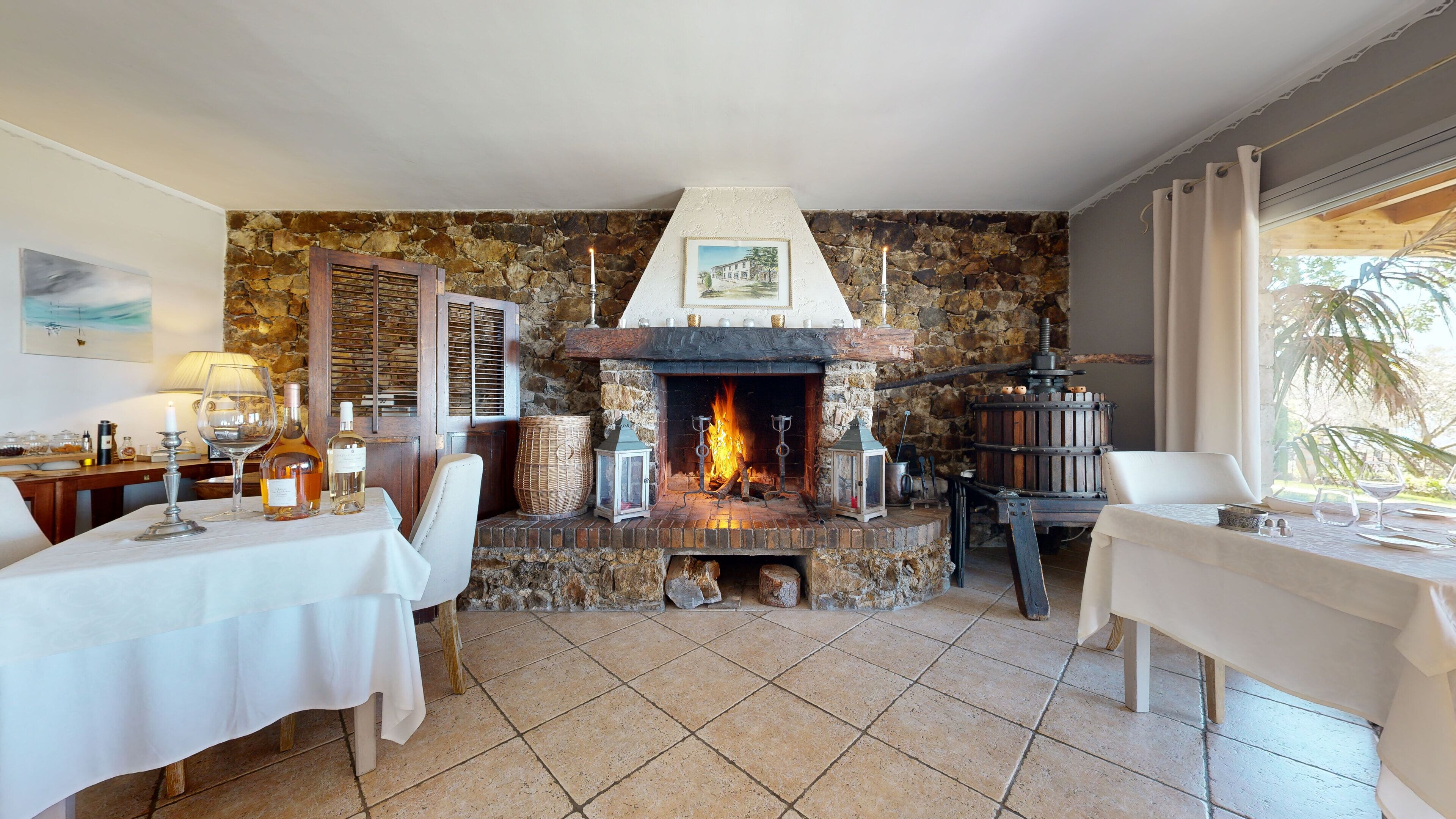 A dining area with a stone fireplace, two tables set for dining, and a view of the outdoors through a window.