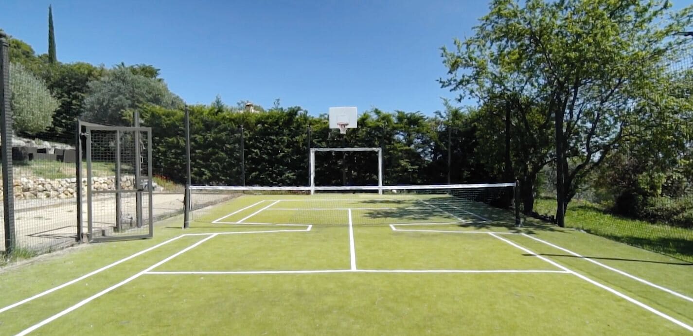 An outdoor tennis court with a net, goalpost, and surrounding greenery.