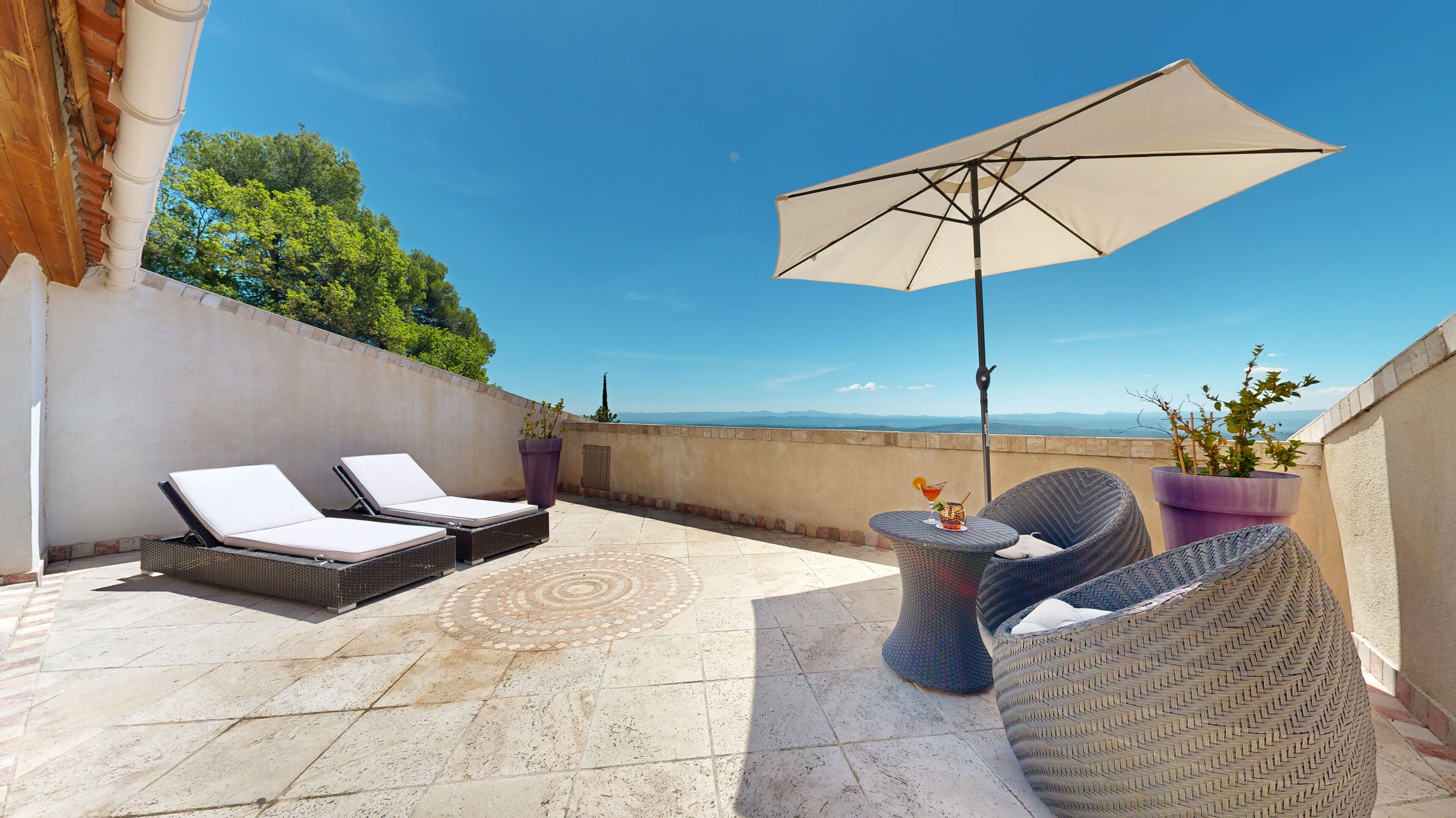 Une terrasse sur le toit, équipée de deux chaises longues, d’une table et d’un parasol.