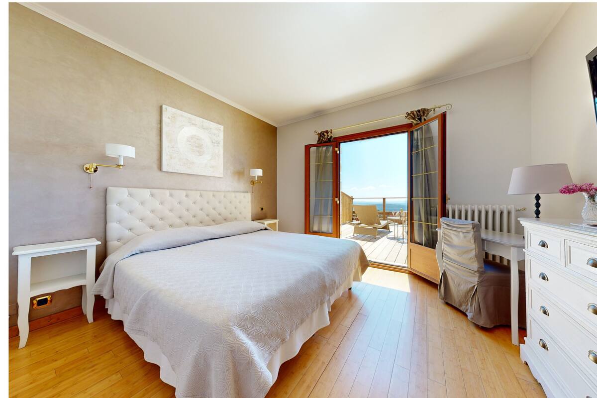 A bedroom with a large bed, a dresser, a TV, and a balcony with a view.