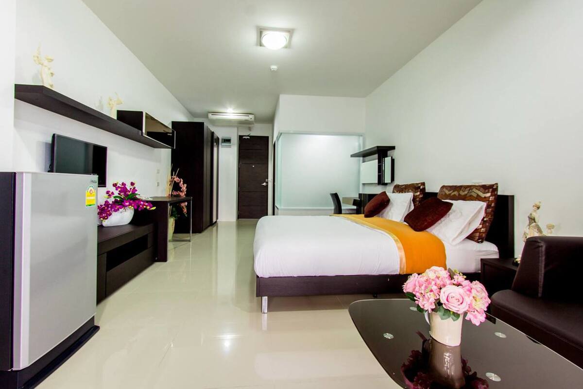 A modern hotel room with a bed, a sofa, a dining table, and a TV.