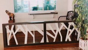 A reception desk with a wooden frame and white geometric patterns, a small elephant figurine, and a potted plant to the right. - The Dlife (Hat Yai)