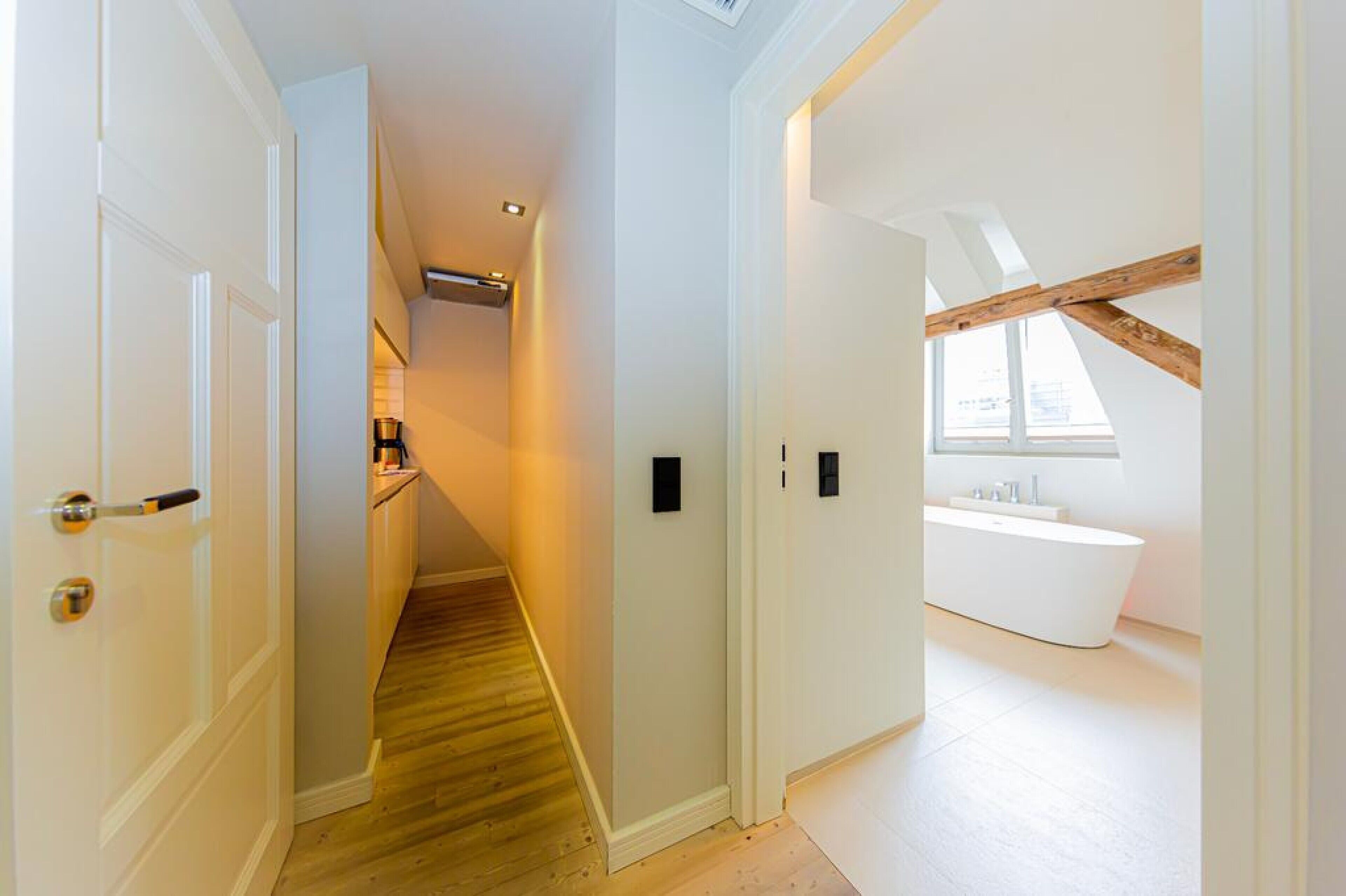 A narrow hallway with wooden flooring leading to a modern bathroom with a freestanding bathtub.