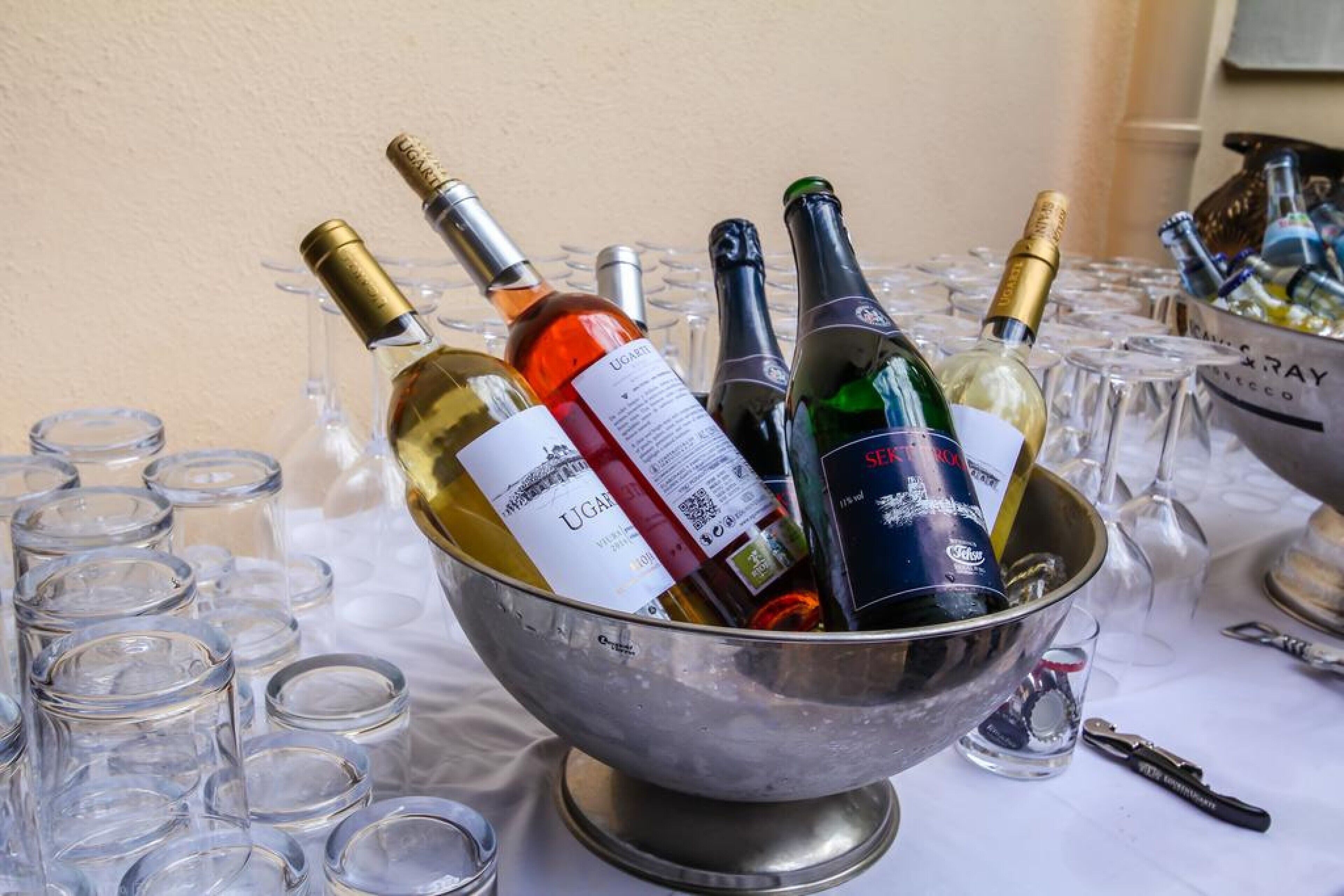 A metal bowl filled with wine bottles and glasses on a table.