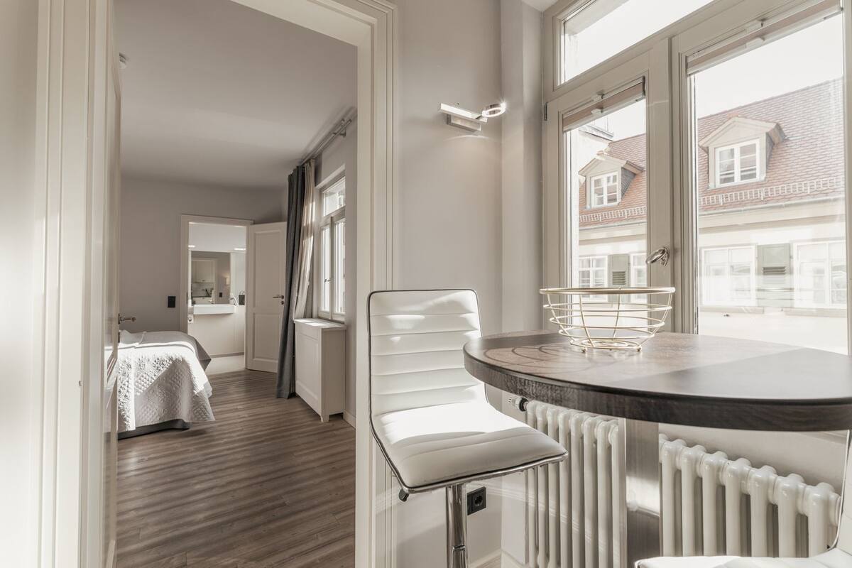 Ein modernes Hotelzimmer mit Holzboden, einem weißen Bett, einem Esstisch mit einem Stuhl und Blick auf Gebäude.