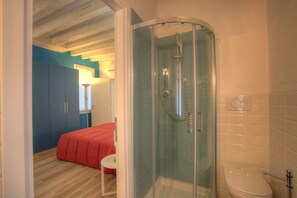 A bathroom with a glass-enclosed shower, a toilet, and a bed with a red blanket. - Ca Sarasina (Venice)