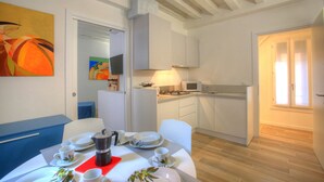 A dining area with a table set for four, a kitchen in the background, and a door leading to another room. - Ca Sarasina (Venice)