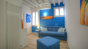 A living room with a blue sofa, a blue ottoman, and a painting on the wall. - Ca Sarasina (Venice)